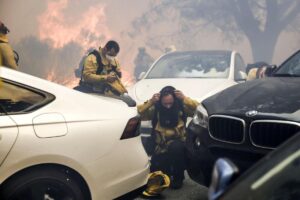 Los bomberos de Los Ángeles ajustan el equipo mientras llegan para combatir el incendio forestal de Palisades, entre los vehículos de los residentes que intentan evacuar la zona en Pacific Palisades, California, Estados Unidos, 07 de enero de 2025