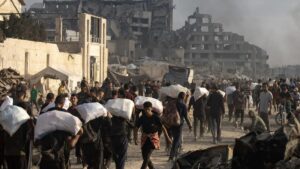 Palestinos desplazados en Jabalia cargan sacos de harina distribuidos por camiones con ayuda humanitaria.