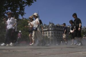Un grupo de turistas camina junto a unos aspersores de agua en una calle de París.