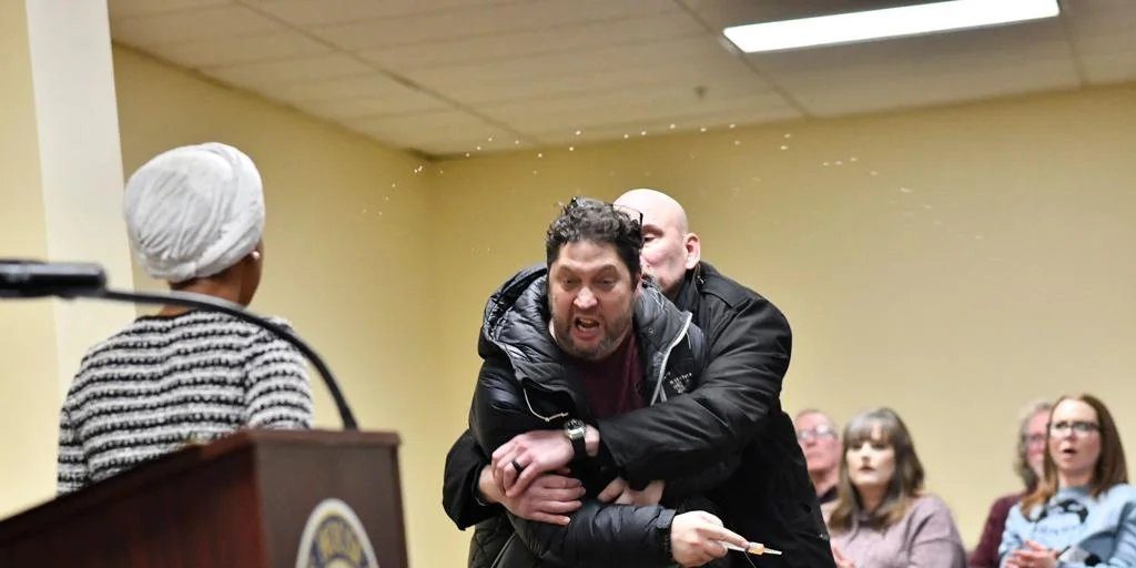 Un hombre rocía con un líquido en una jeringuilla a la congresista demócrata Ilhan Omar durante un discurso en Mineápolis