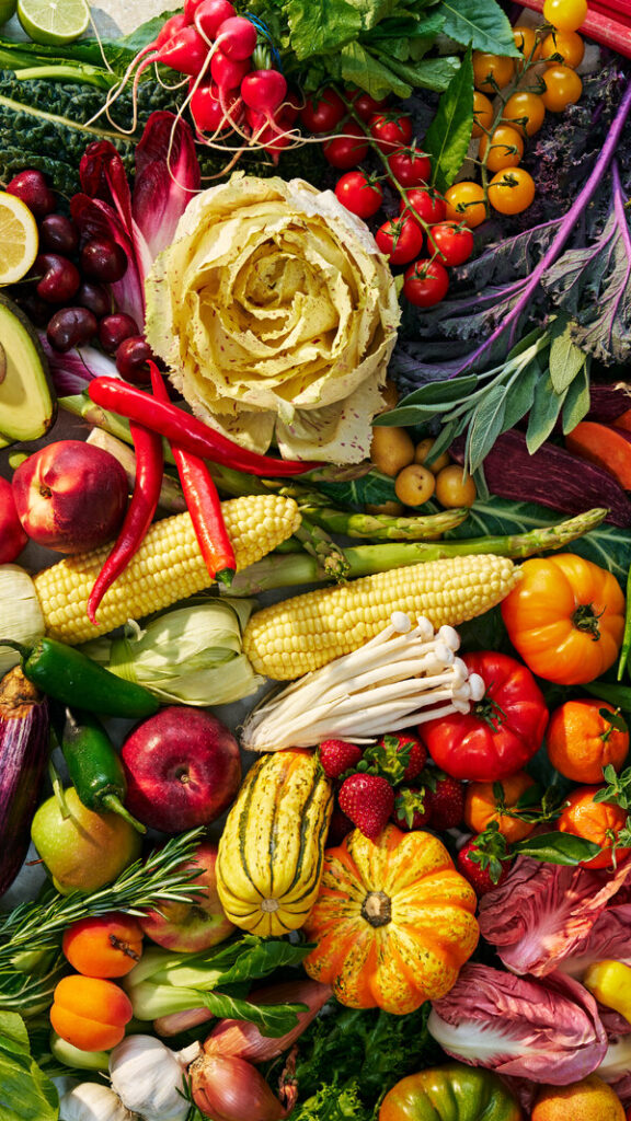 Hermosos productos agrícolas, como tomates de color rojo vivo, manzanas y calabazas brillantes, hierbas aromáticas y una col, yacen en un revoltijo ingeniosamente ordenado.