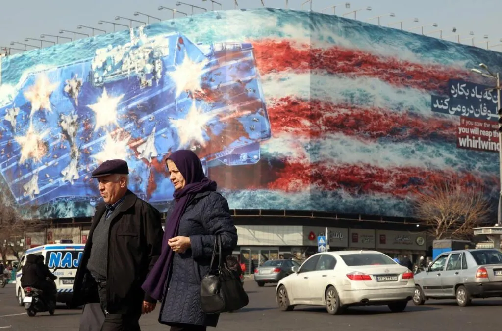 Iraníes caminan cerca de un enorme cartel antiestadounidense colgado en la plaza Enqelab de Teherán, Irán, este martes