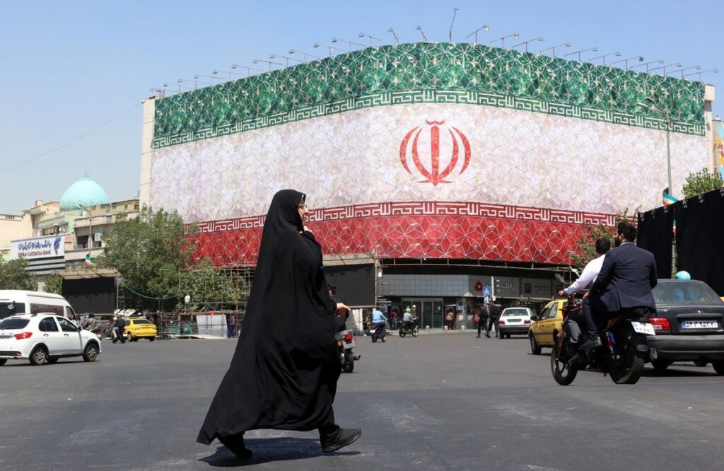 Una mujer pasa frente un cartel gigante con la bandera de Irán, este doming en Teherán.